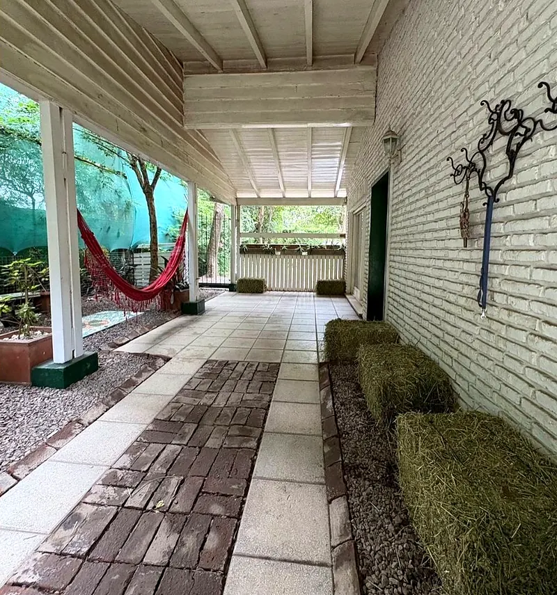 Galería techada de la casa con hamaca roja y canteros