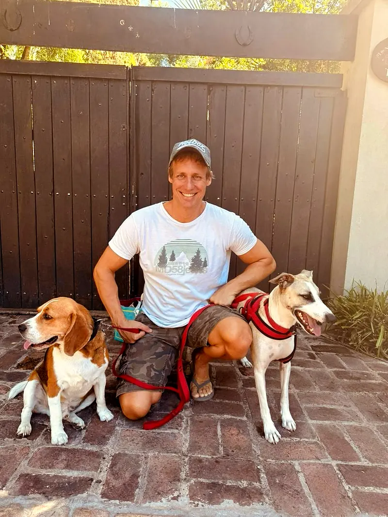 Marcelo agachado sobre un piso de ladrillo con un beagle y otro perro con correa
