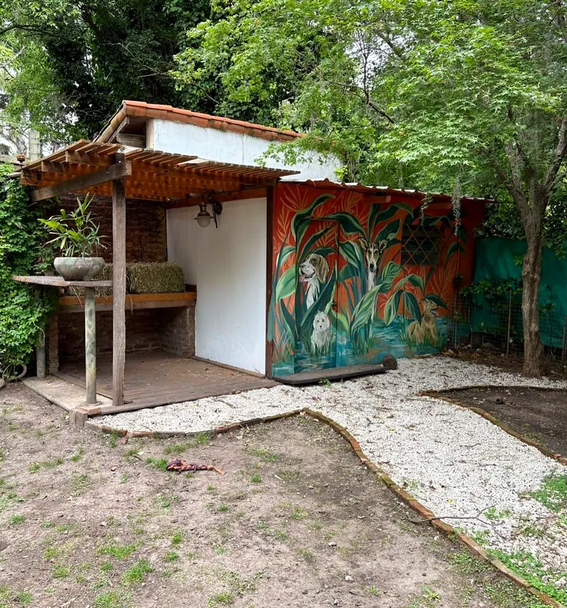 Quincho con mural de perros pintado en la pared, rodeado de árboles